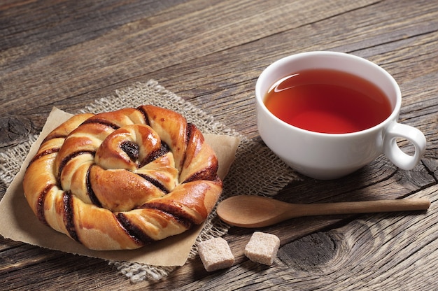 Cup of hot tea and sweet bun with jam on old wooden table