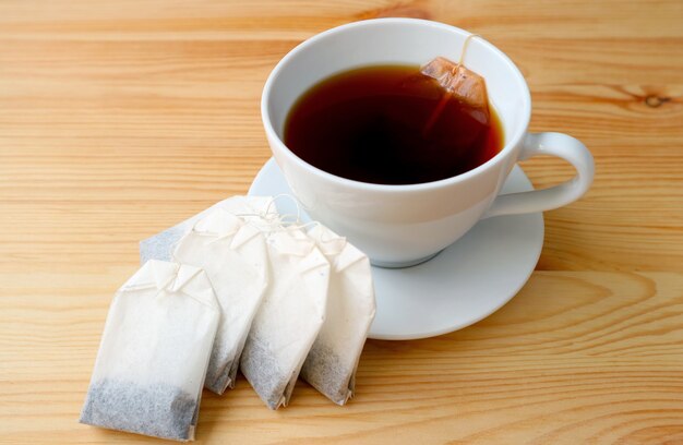 Tazza di tè caldo con un mucchio di bustine di tè isolate su un tavolo di legno