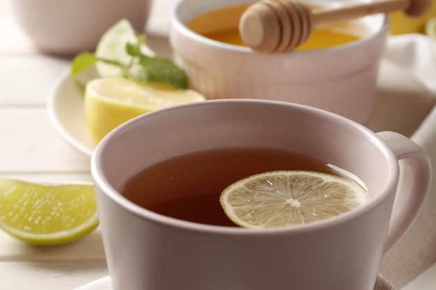 Cup of hot tea with honey, ginger, lemon and mint on a white wooden background