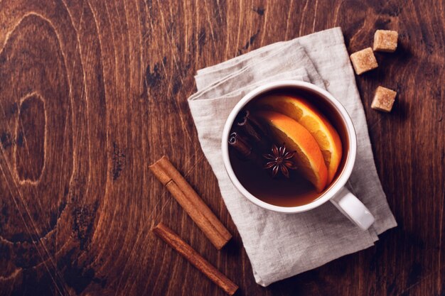 Cup of hot tea with orange and spices on a rustic brown table. Close-up