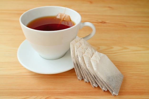 Cup of hot tea with tea bags served on wooden table