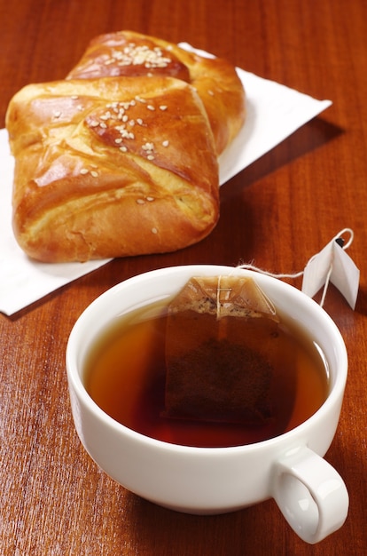 Cup of hot tea with teabag and sweet buns on table