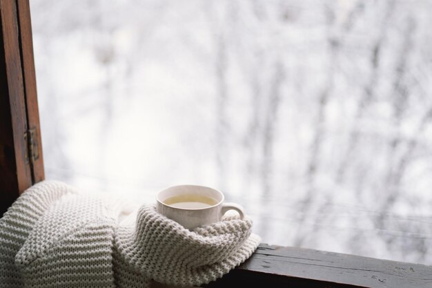 Чашка горячего чая с теплым свитером на винтажном деревянном подоконнике