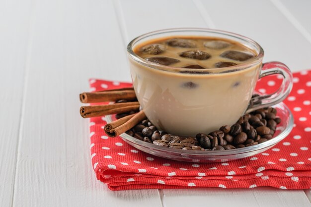 A Cup of iced coffee and cinnamon on a red cloth on a white wooden table. Refreshing and invigorating drink of coffee beans and milk.