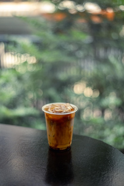 A cup of iced coffee with ice cubes on a black table.