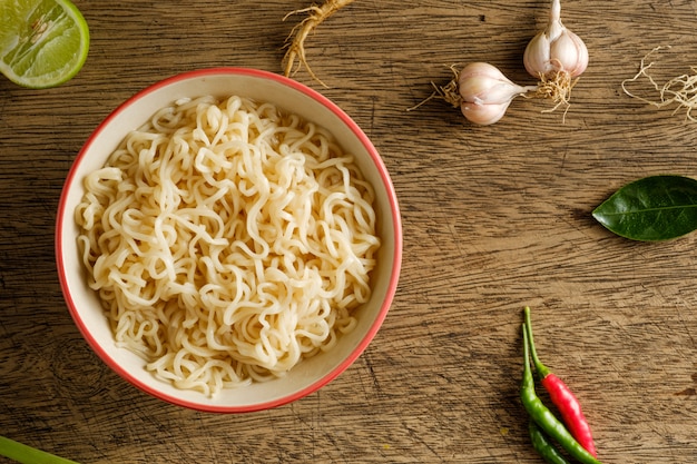 A cup of instant noodles placed on a wooden table With lime,chilli,lemon grass and garlic as ingredients  noodle