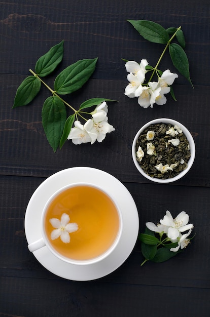 Photo cup of jasmine tea and jasmine flowers on dark wooden background. top view.