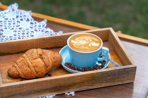 A cup of latte art coffee and croissant on a table on natural defocused background in garden