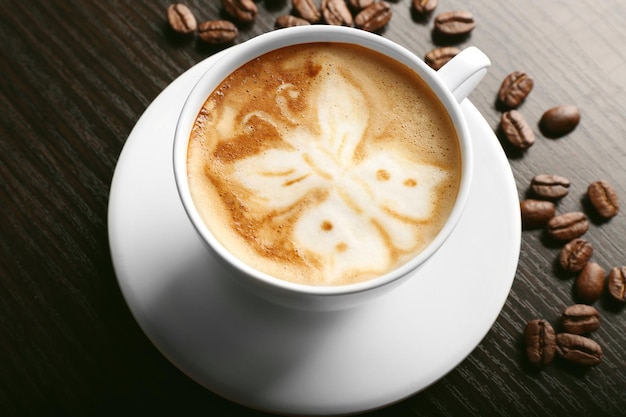 Cup of latte art coffee with grains on wooden background