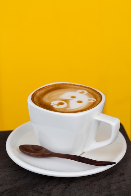 Cup of latte coffee like face bear on yellow background