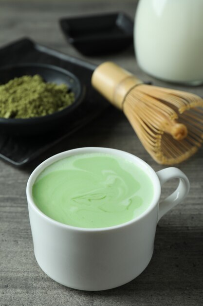 Cup of matcha latte and accessories for making on gray textured table