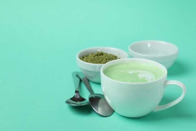 Cup of matcha latte and accessories for making on mint background