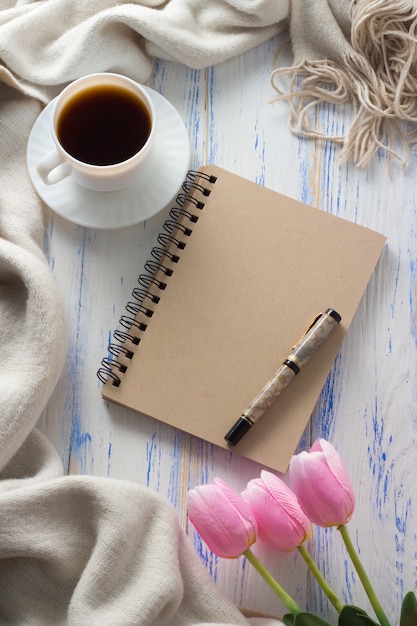 Cup met koffie, Kladblok, tulpen, pen op witte houten tafel. Concept van de lente