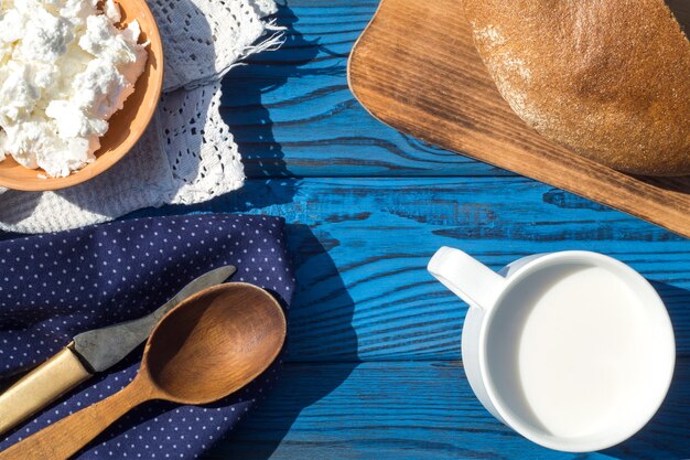 A cup of milk, cottage cheese and bread on a table of blue boards. Top view