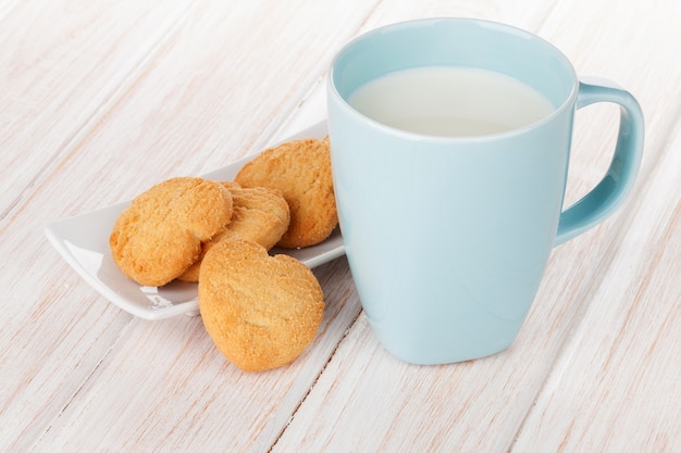 Cup of milk and heart shaped cookies on white wooden table