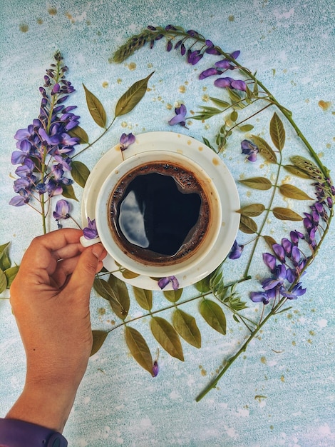 Cup of morning hot black coffee on a blue background. white flowers as a daily ritual. Top view