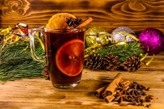 Cup of mulled wine with cinnamon, christmas decorations and fir tree branches on rustic wooden table