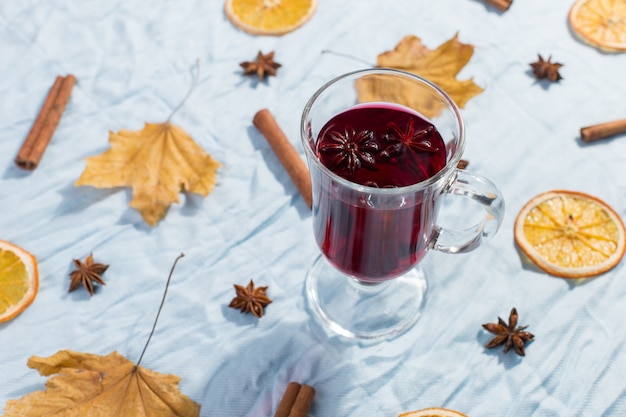 A cup of mulled wine with spices, dry leaves and oranges on the table. Autumn mood, a method to keep warm in the cold, copyspace, morning light.