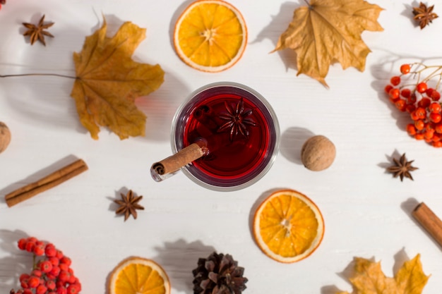 A cup of mulled wine with spices, dry leaves and oranges on the table. Autumn mood, a method to keep warm in the cold, morning light, flat lay.