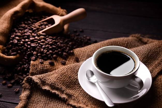写真 一杯のコーヒーと古い木製の背景に黄麻布の袋のコーヒー豆