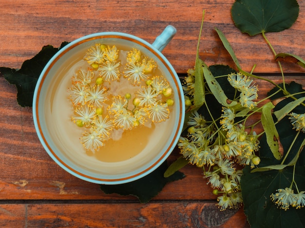 緑茶とリンデンの木製の背景、便利なリンデンの花民間療法の概念のカップ