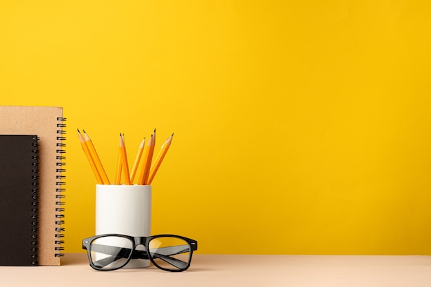 Cup of pencils and notepads on desk against yellow background