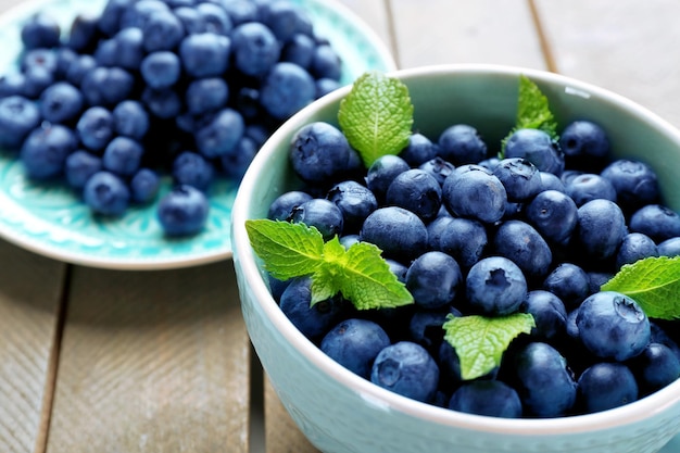 Cup and plate with fresh blueberries on wooden table close up