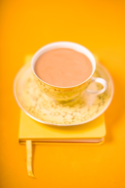 Cup and saucer and coffee with milk on a yellow background vertical