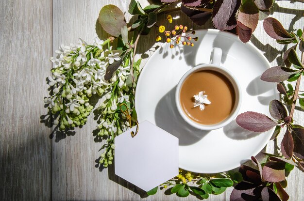 Cup on a saucer with mockup an empty white card framed by branches of burgundy and green leaves