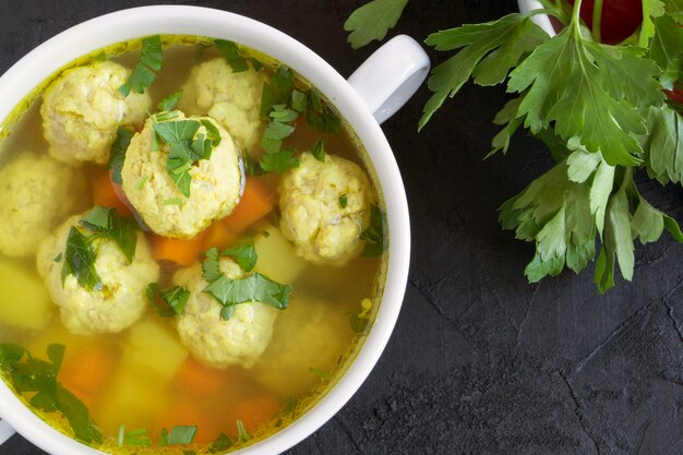 A cup of soup with meatballs and vegetables