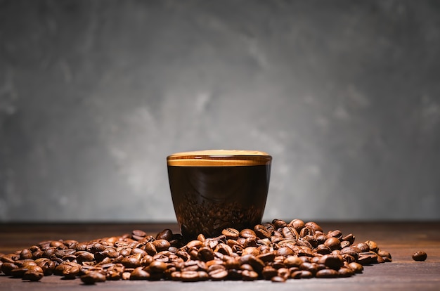 Tazza di caffè espresso forte, primo piano, messa a fuoco selettiva. tazza con caffè con schiuma aromatica e fagioli tostati su un tavolo grigio