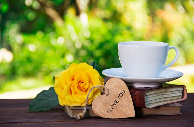 Tazza di tè estivo sulla pila di libri e fragrante rosa gialla