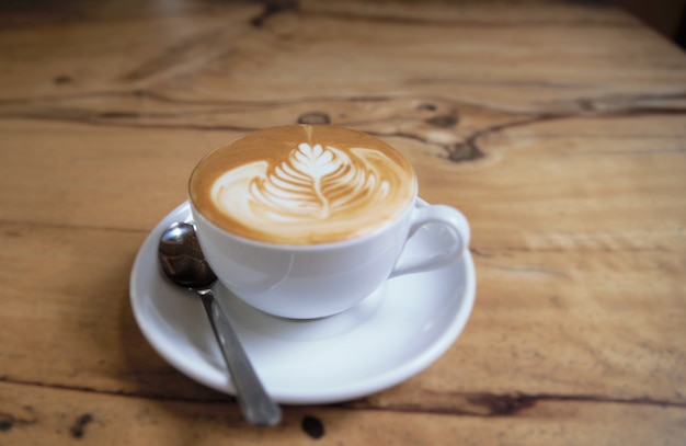 Cup of tasty cappuccino is standing on the wooden textured table. Cappuccino is in the white big cup.