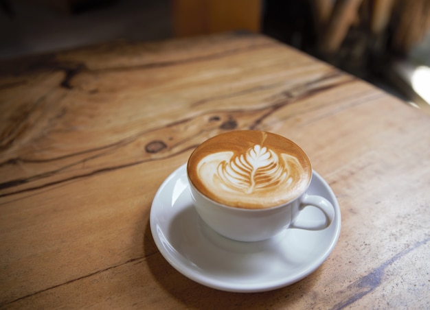 Cup of tasty cappuccino is standing on the wooden textured table. Cappuccino is in the white big cup.