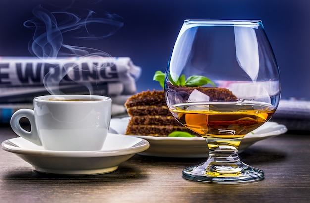 Tazza di gustosa bevanda cognac caffè torta di miele e giornale.