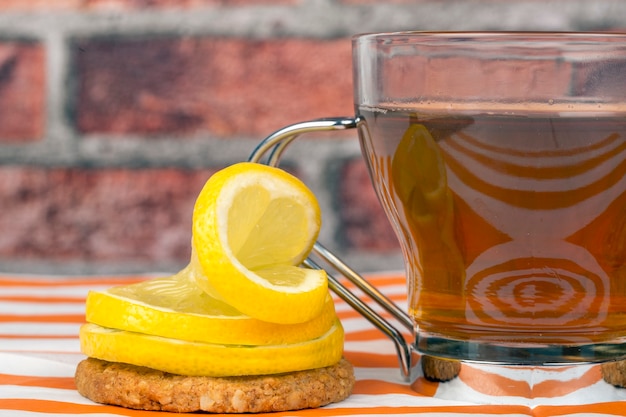 Photo cup of tea accompanied by lemon slices decoratively placed on an oatmeal cookie on a brick wall background