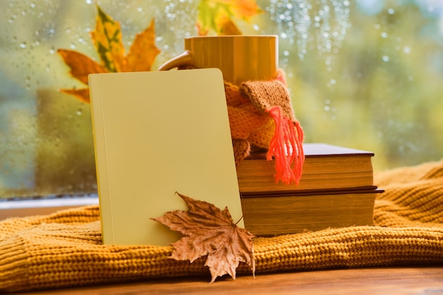 Tazza di tè, foglie autunnali, libri, quaderno e plaid a maglia rossa sul tavolo di legno