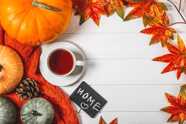 Cup of tea autumn leaves and pumpkins on a white wooden background copy space for text Cozy and warm autumn flatlay