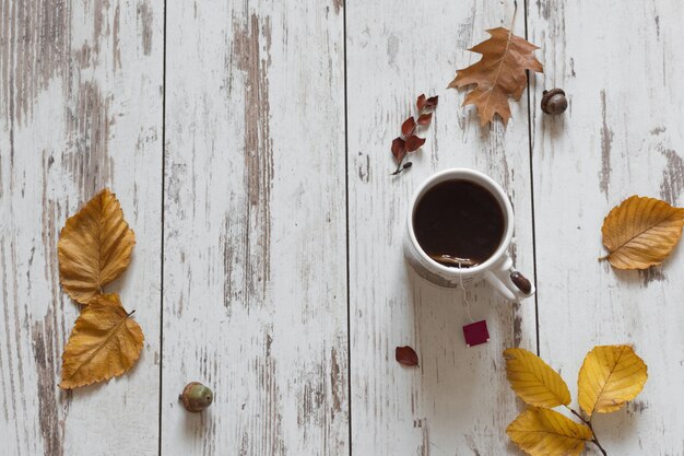 Cup of tea, autumn leaves on wooden table top view.