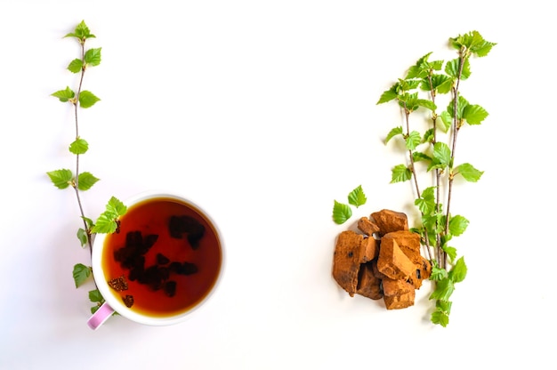 Tazza di tè di betulla chaga funghi e pezzi di funghi chaga schiacciati per la preparazione del tè isolato su uno sfondo bianco.