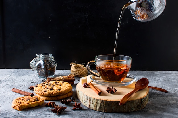 Tazza di tè, biscotti, cannella, anice su sfondo scuro