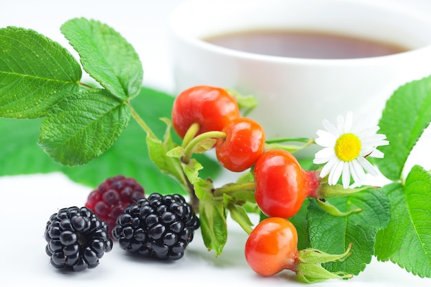 Photo cup of tea, blackberry,raspberry and rosehip berries with leaves