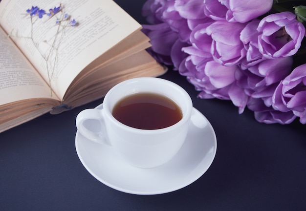 Чашка чая, книга и фиолетовые тюльпаны на столе