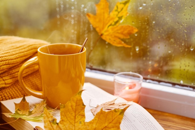 Cup of tea books autumn leaves and candle on window sill at home