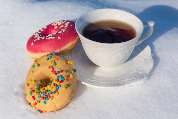 外の雪の背景にドーナツと朝食のお茶のカップ