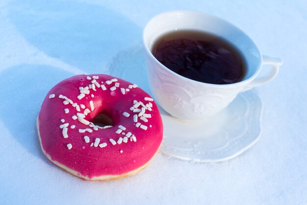 雪の背景にドーナツと朝食のお茶のカップ