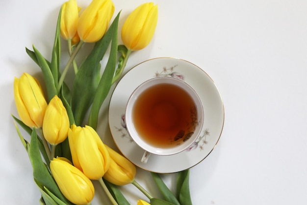 A cup of tea and bunch of yellow tulips on white background Concept of holiday birthday