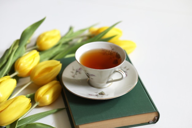 A cup of tea and bunch of yellow tulips on white background Concept of holiday birthday