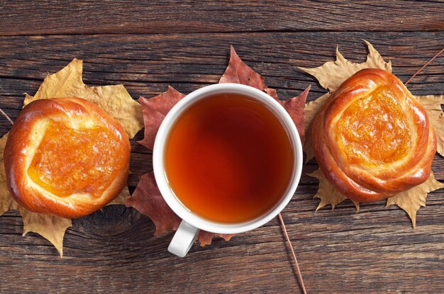 Cup of tea and buns with apricot jam on dark wooden table top view