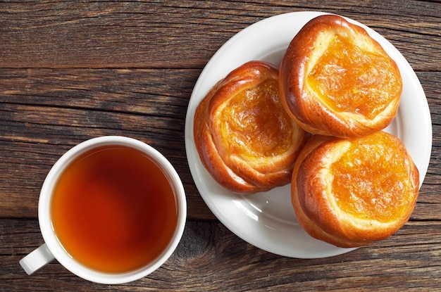 Cup of tea and buns with apricot jam on old wooden table top view